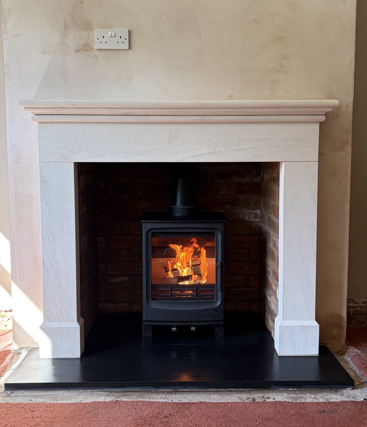 Lit stove installed in a stone fireplace with black hearth